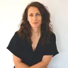 Danielle Spigariol, longs cheveux bruns bouclés, un léger sourire, haut noir, devant un mur blanc