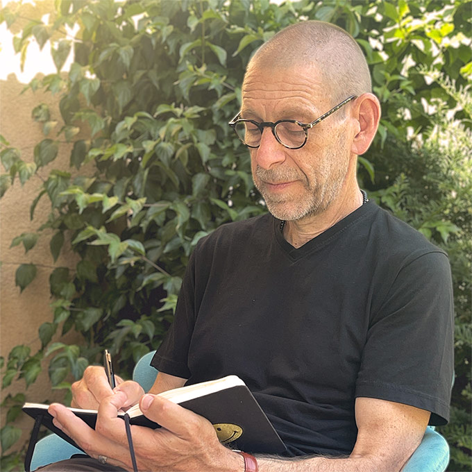 Denis Jaccard écrit dans un carnet, assis au jardin